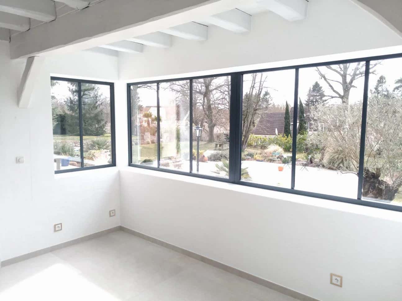 Pièce rénovée entièrement blanche ouverte sur le jardin par de grandes baies vitrées d'angle
