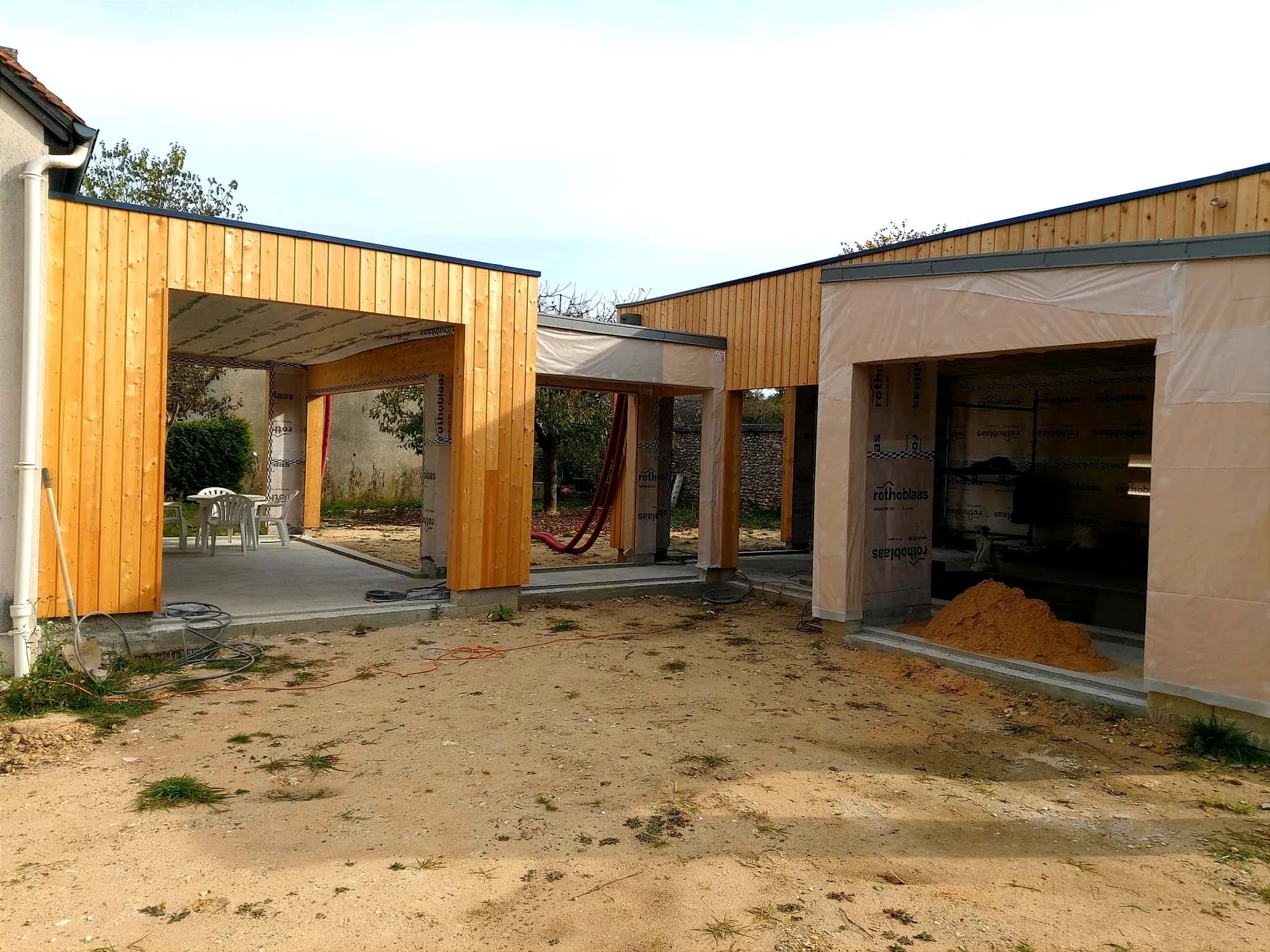 Double préau en bardage bois relié à une extension, sol en cours de préparation