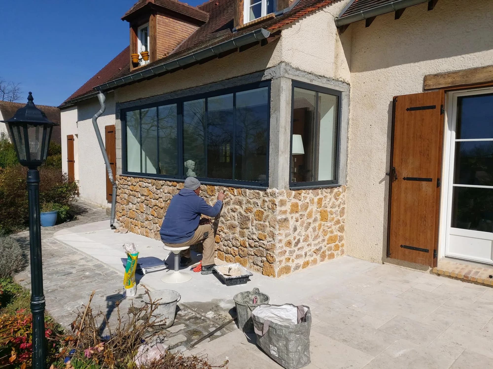 Artisan appliquant l'enduit sur le soubassement en pierre d'une maison ancienne rénovée