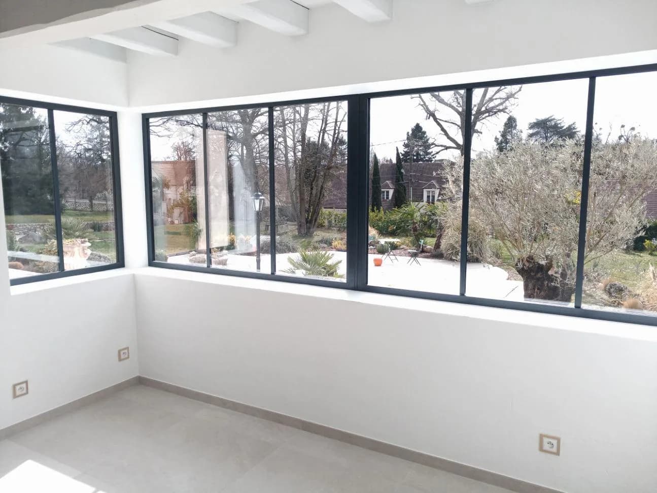 Séjour rénové aux murs blancs, baies vitrées d'angle ouvrant sur un jardin arboré