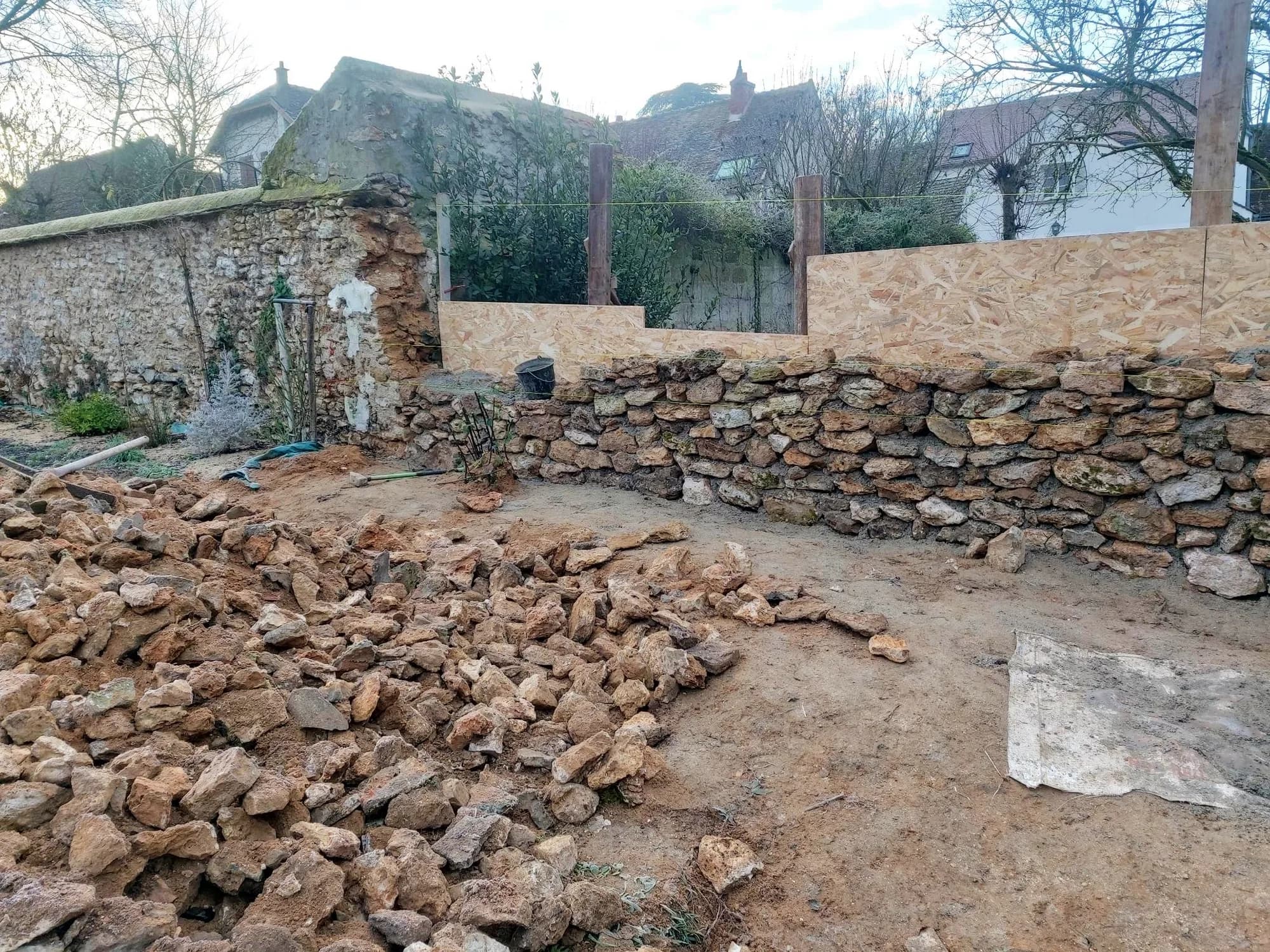Mur en pierre en cours de reprise avec gravats et pierres de récupération au sol