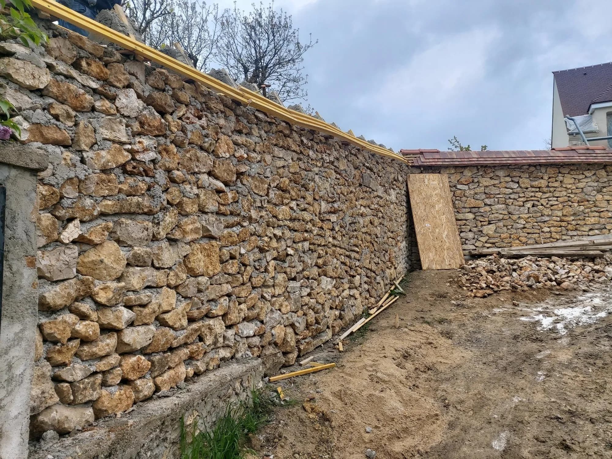 Long mur de clôture en pierre restauré et rejointoyé, arase en cours de protection