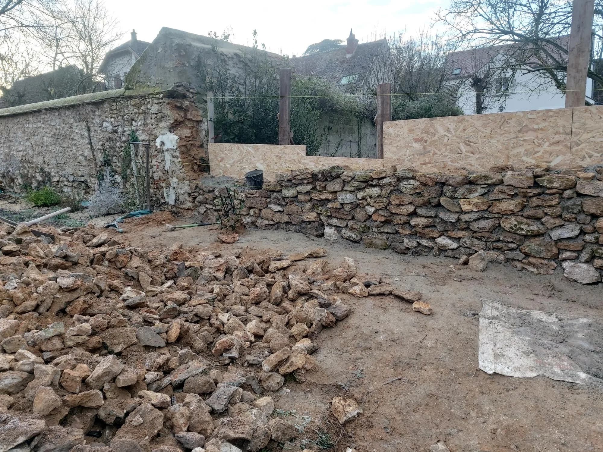 Mur en pierre sèche en cours de remontage, pierres triées au premier plan