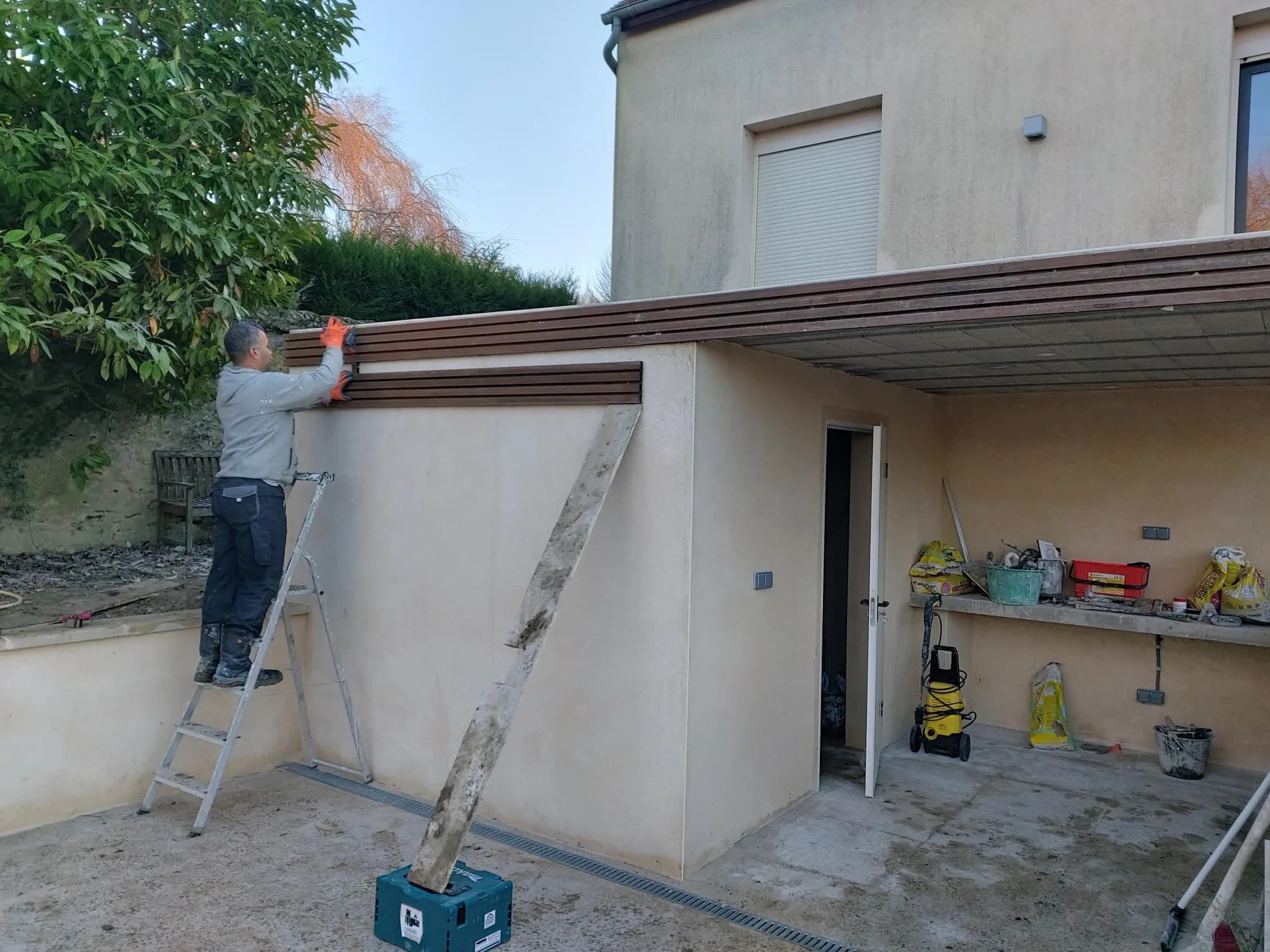 Carport neuf en cours de finition, artisan sur une échelle appliquant l'enduit
