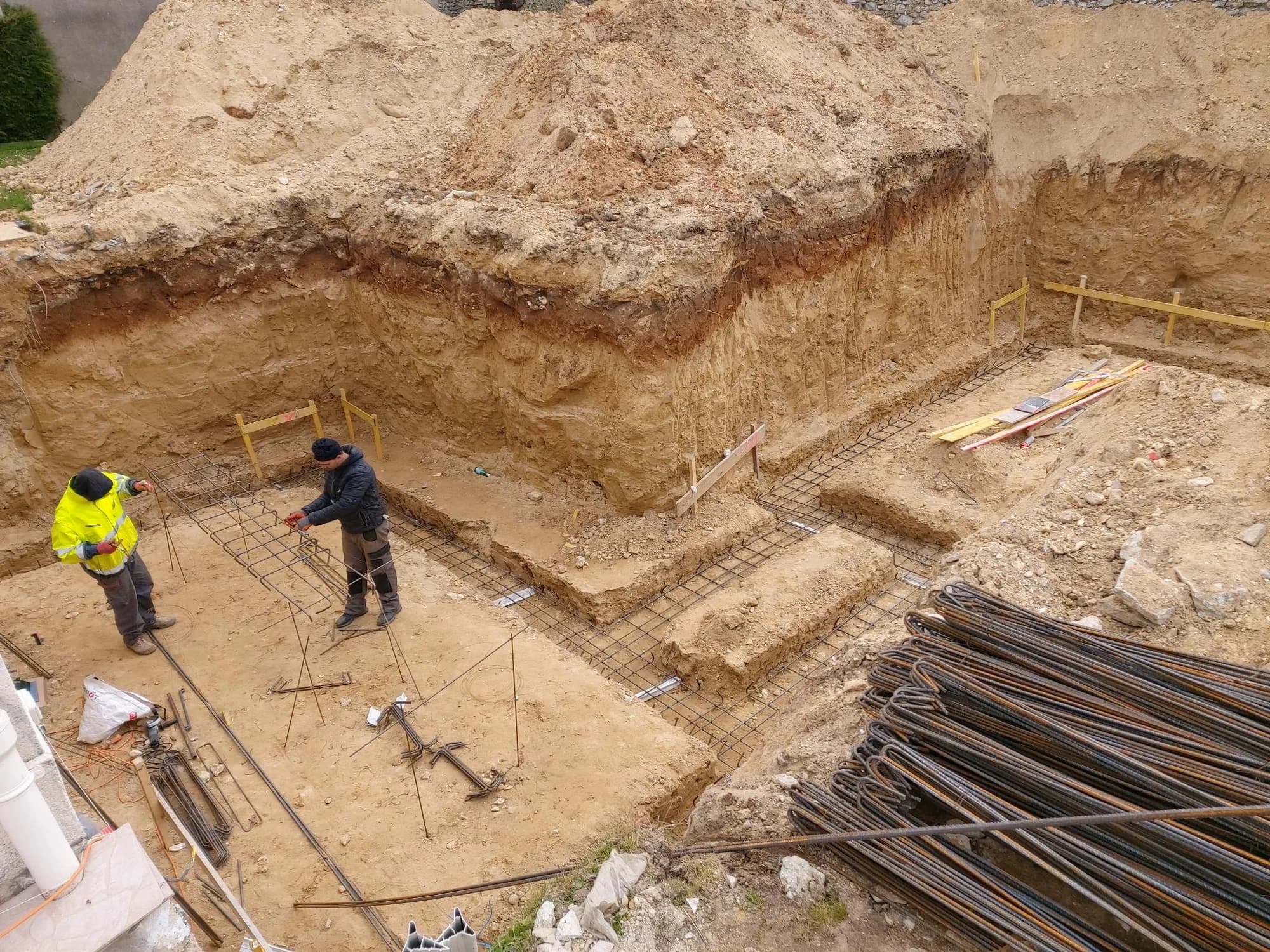 Deux compagnons ferraillent les semelles de fondation d'une maison, fouilles ouvertes