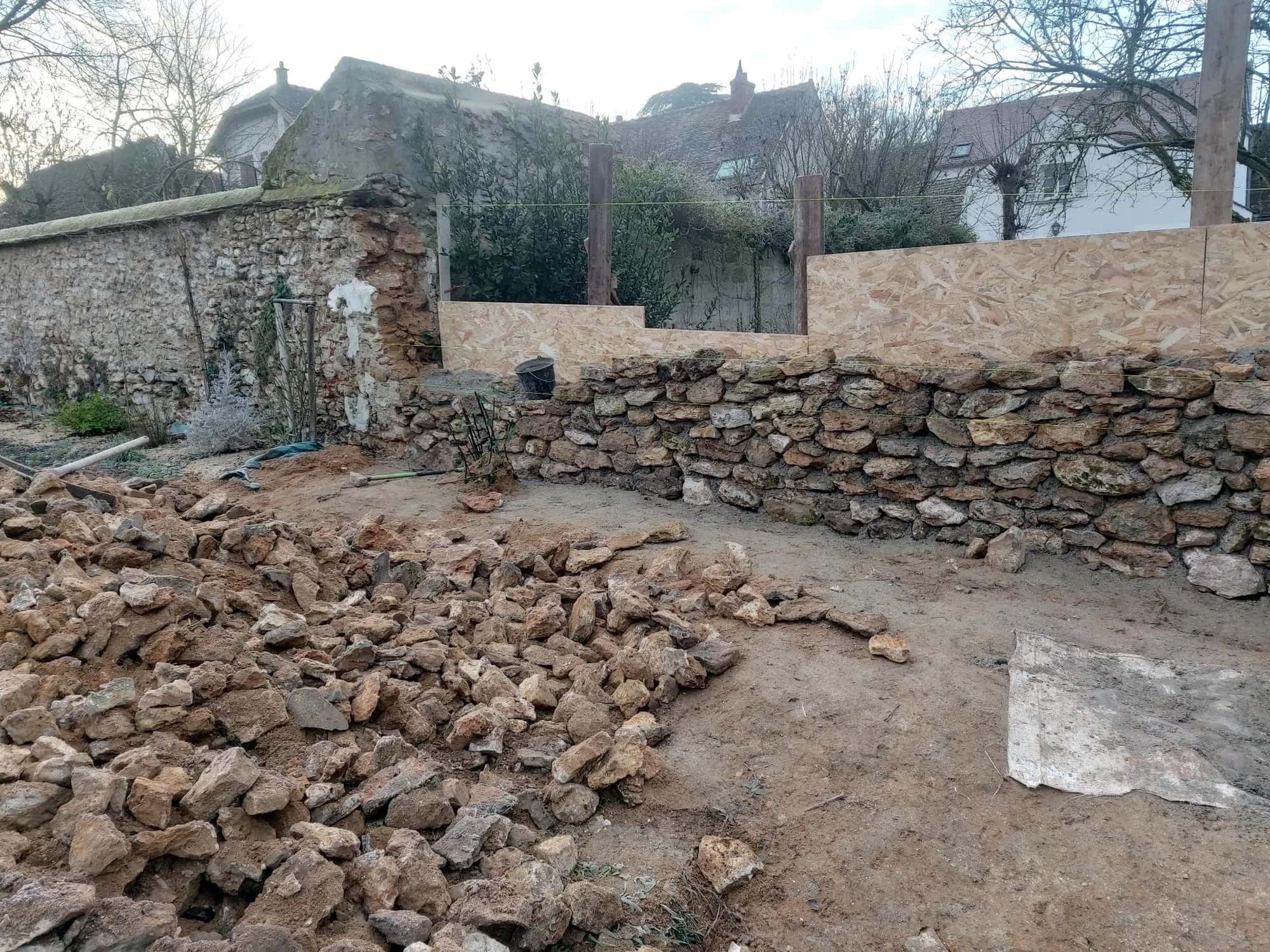 Mur en pierre sèche en cours de remontage, pierres triées au premier plan