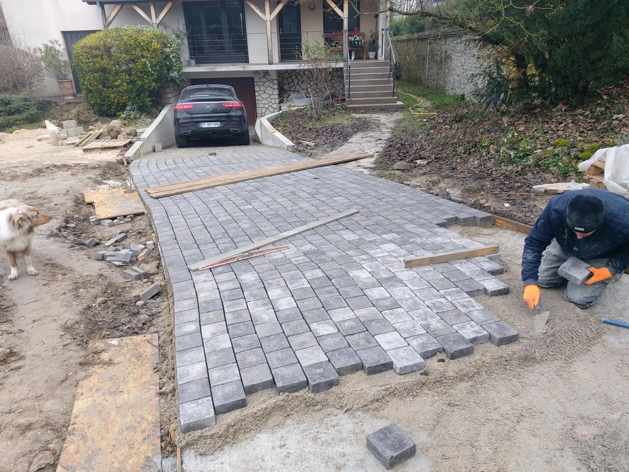 Pose de pavés en pierre sur une descente de garage, artisan agenouillé au travail