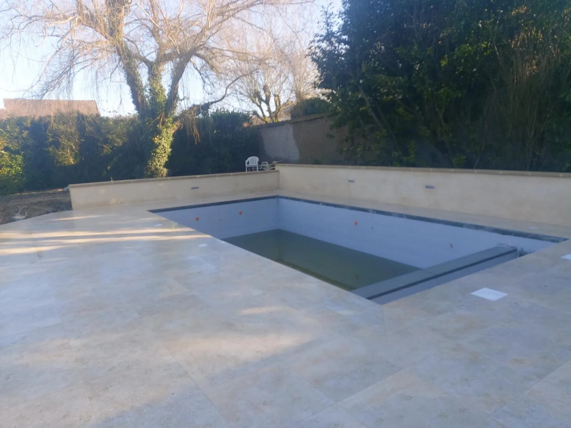 Piscine terminée avec sa plage en pierre reconstituée dans un jardin clos