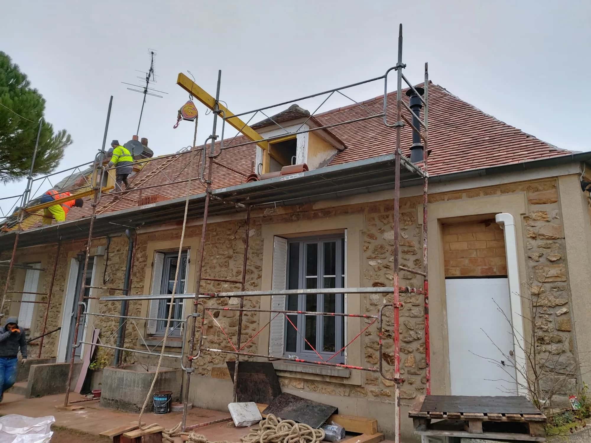 Toiture de maison ancienne en réfection avec échafaudage et grue de chantier