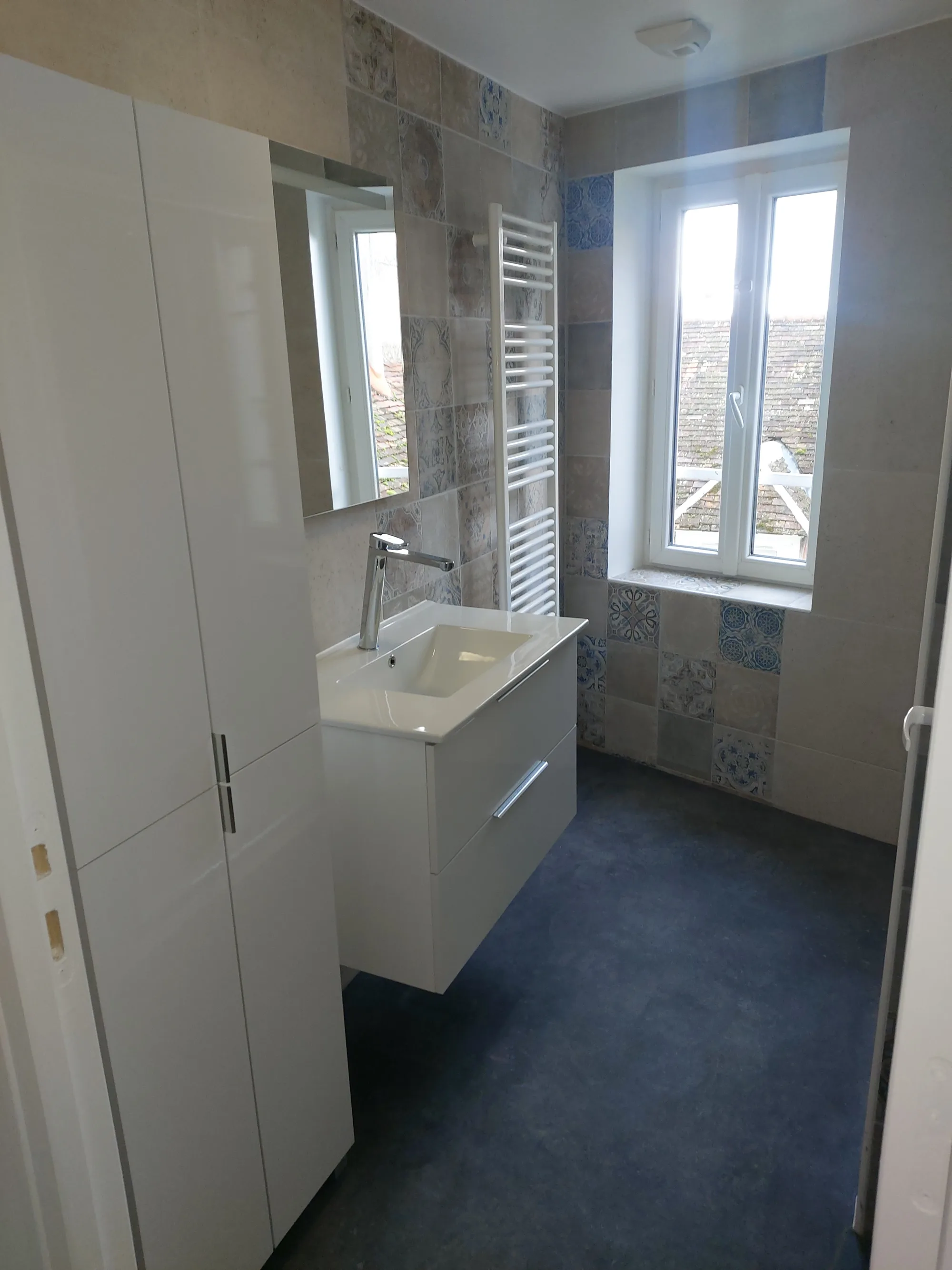 Salle de bain rénovée avec meuble vasque suspendu blanc, sèche-serviettes et carrelage à motifs